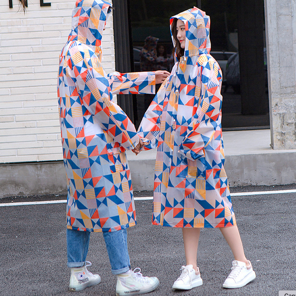 Une femme et un homme posent dans la rue. Ils portent une veste longue transparente avec motif géométrique coloré. Ils portent aussi des baskets blanches.