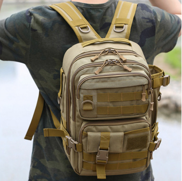 Un homme pose dans la nature. Il porte un tee-shirt vert camouflage. Il porte aussi un sac à dos imperméable étanche beige. 