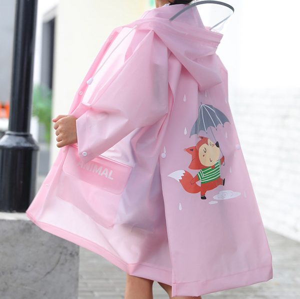Une petite fille pose dans la rue. Elle porte une veste imperméable longue rose avec un dessin de renard tenant un parapluie dans le dos. 
