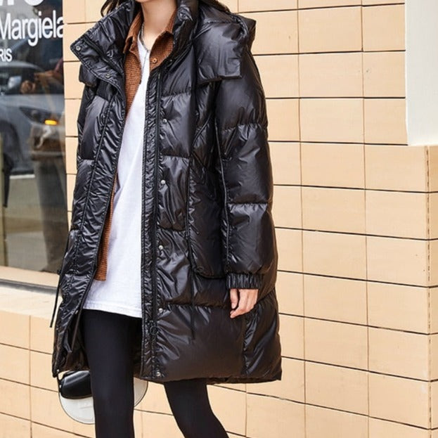 Une femme pose devant un magasin. Elle porte un tee-shirt blanc, une chemise marron et un legging noir. Elle porte aussi un manteau imperméable doudoune noire brillante.