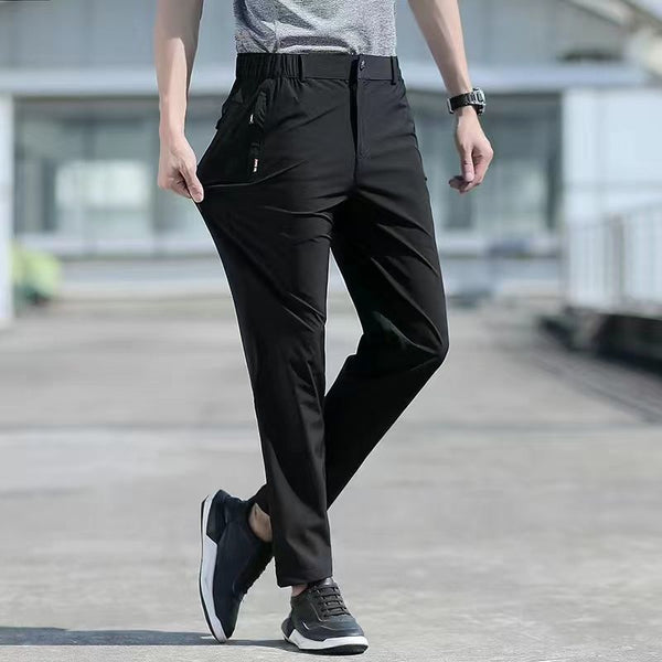 Un homme pose dans la rue. Il porte un tee-shirt gris, des baskets noirs et un pantalon imperméable noir extensible ajusté.