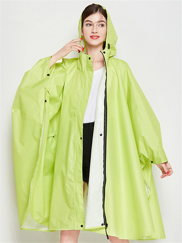 Une femme pose dans un tee-shirt blanc et un short noir. Elle porte aussi une veste imperméable poncho long vert citron. Elle est brune et a un rouge à lèvres rouge et du vernis rouge.