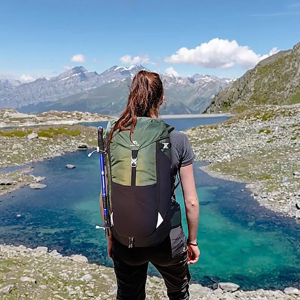 Une femme pose devant un lac de montagne avec un sac à dos imperméable kaki de randonnée à grande capacité. 