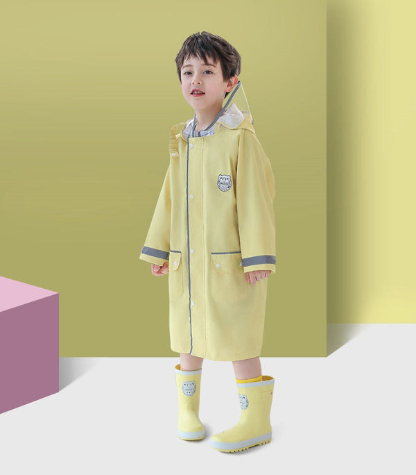 Un garçon pose dans une veste imperméable à capuche et écusson marin. Il porte aussi des bottes de pluie jaune. 