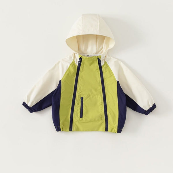 Une veste colorblock verte, beige et bleu marine est posé sur un fond beige. Elle a deux fermetures éclair sur le devant et une poche zippée.