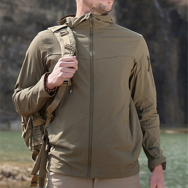 Un homme pose dans la nature. Il porte un pantalon beige, un sac à dos beige et une veste imperméable légère, respirante et à séchage rapide beige.