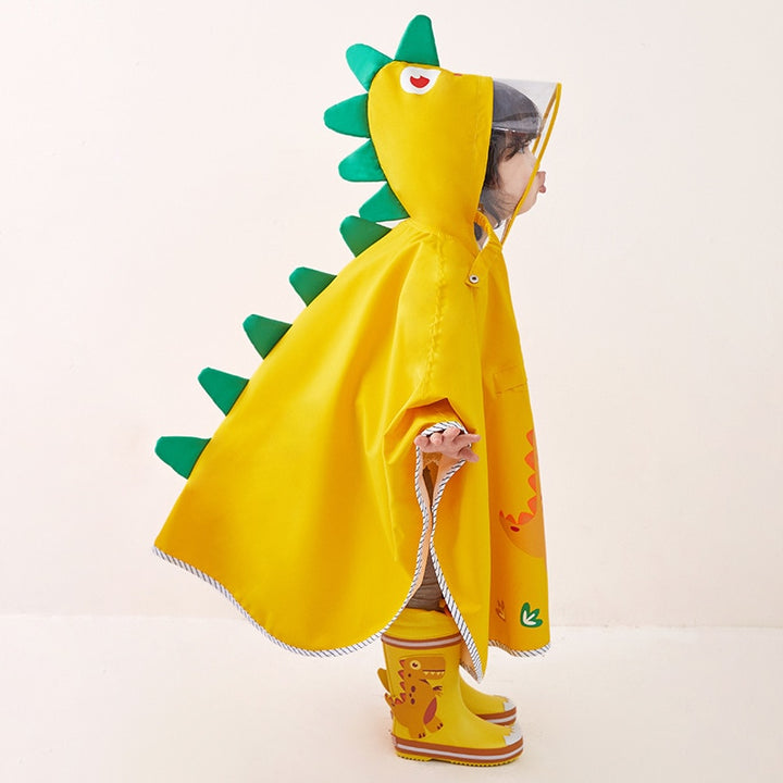 Une enfant pose dans un poncho imperméable jaune dinosaure. Elle porte aussi des bottes de pluie jaunes avec des dinosaures dessus.