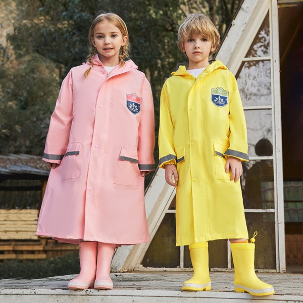Deux enfants posent devant une cabane en bois. Ils portent tous les deux des bottes de pluie assorties à un long ciré imperméable. Le garçon porte un ciré jaune et la fille un ciré rose.